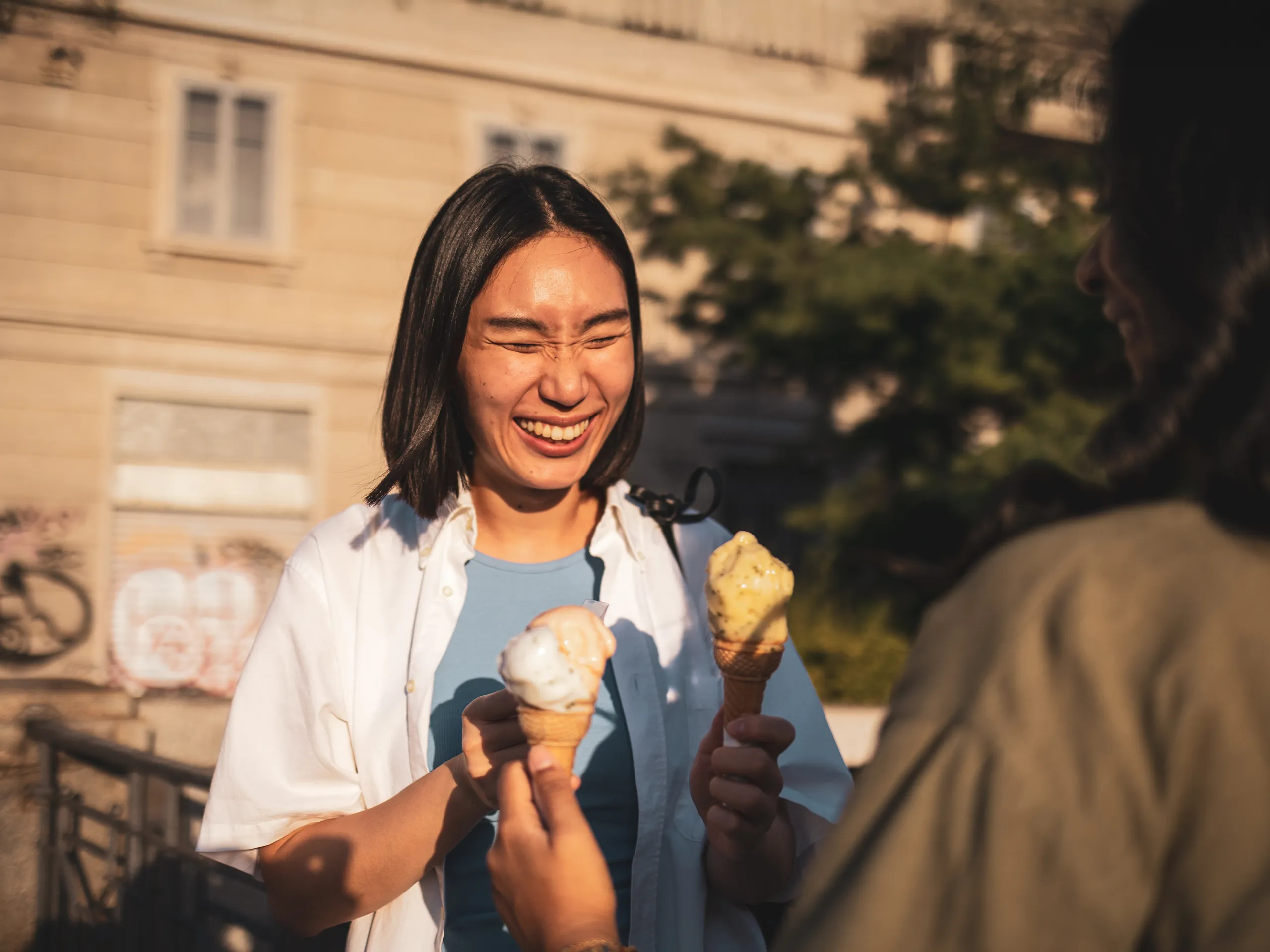 Lachende Frau hält zwei Eiswaffeln in der Abendsonne