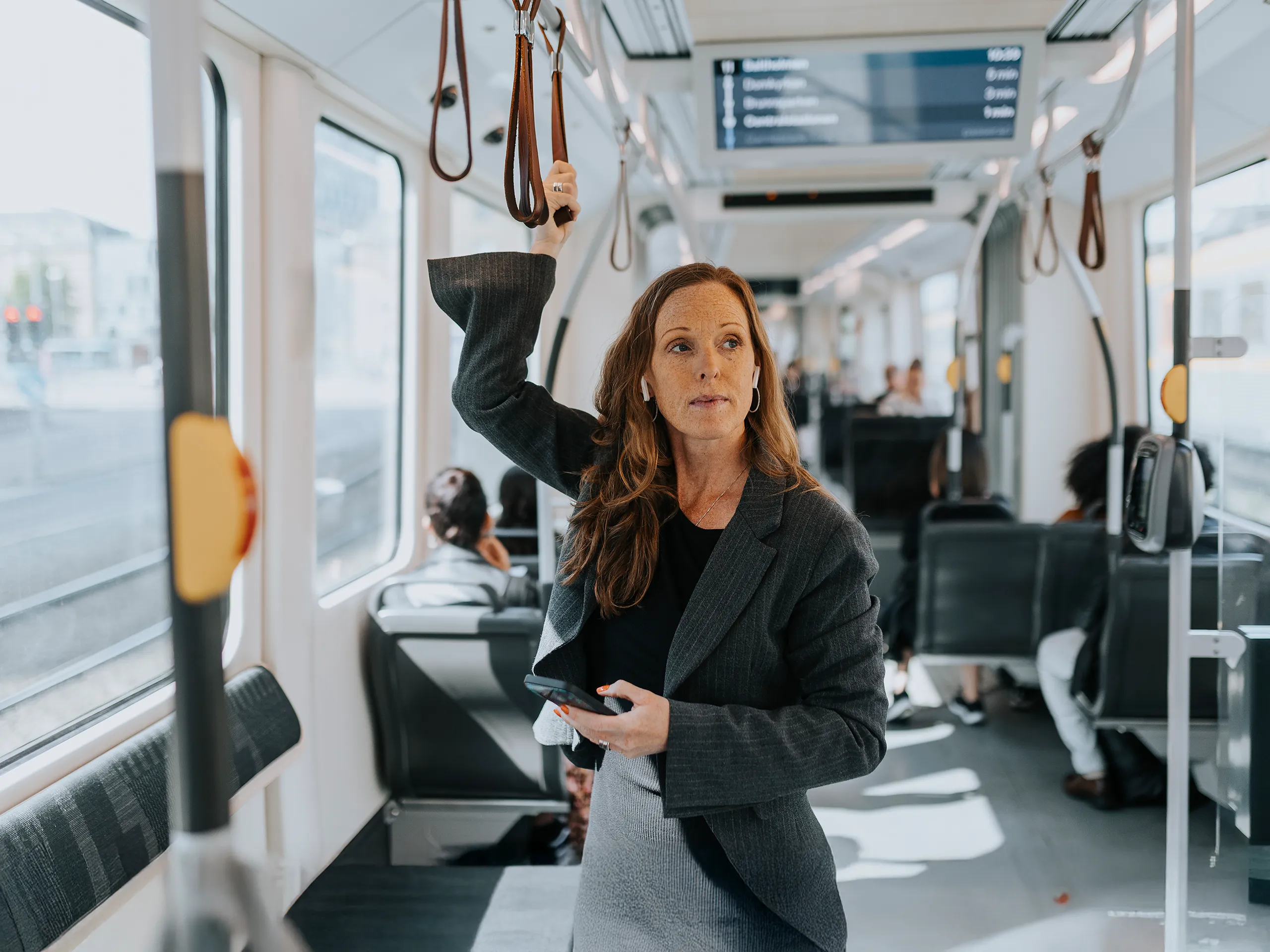 Geschäftsfrau mit Smartphone fährt in einer Straßenbahn.