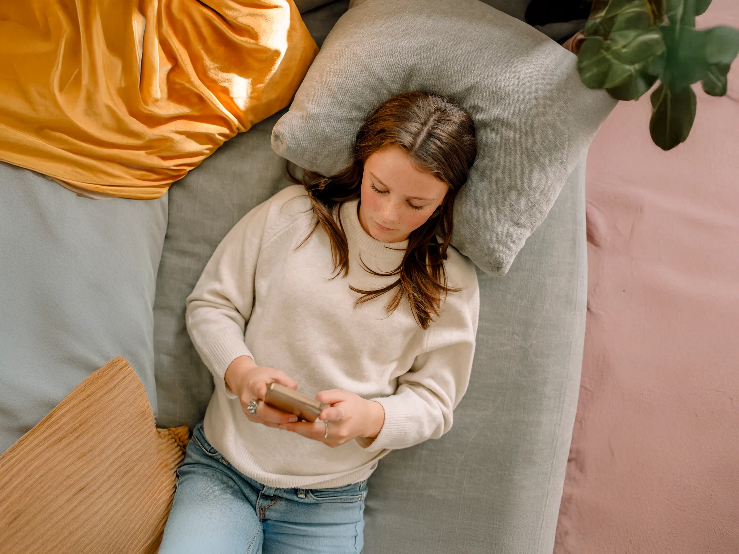 Mädchen liegt auf Bett und schaut auf Smartphone