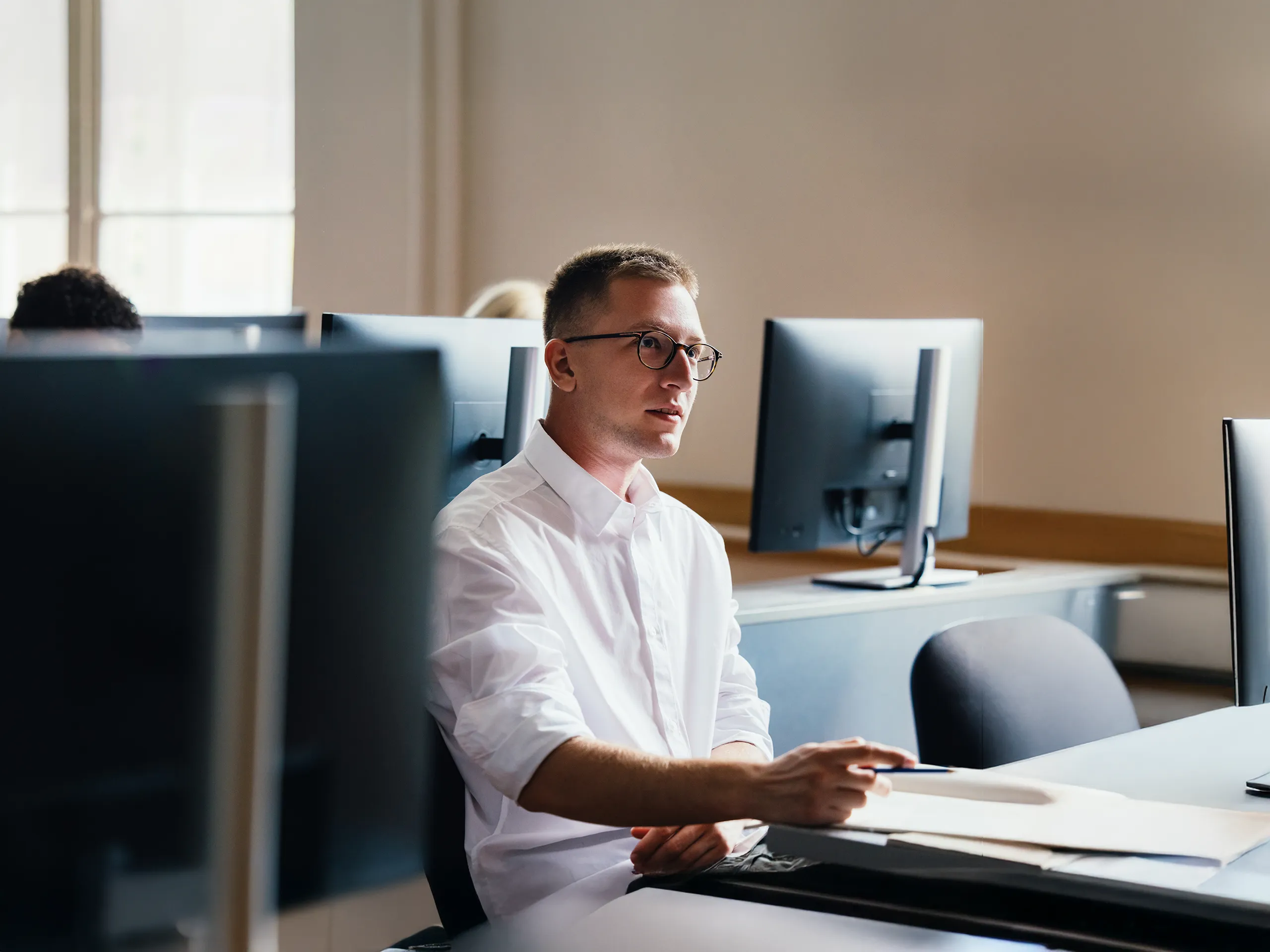 Mann mit Brille sitzt aufmerksam in einem Computerraum