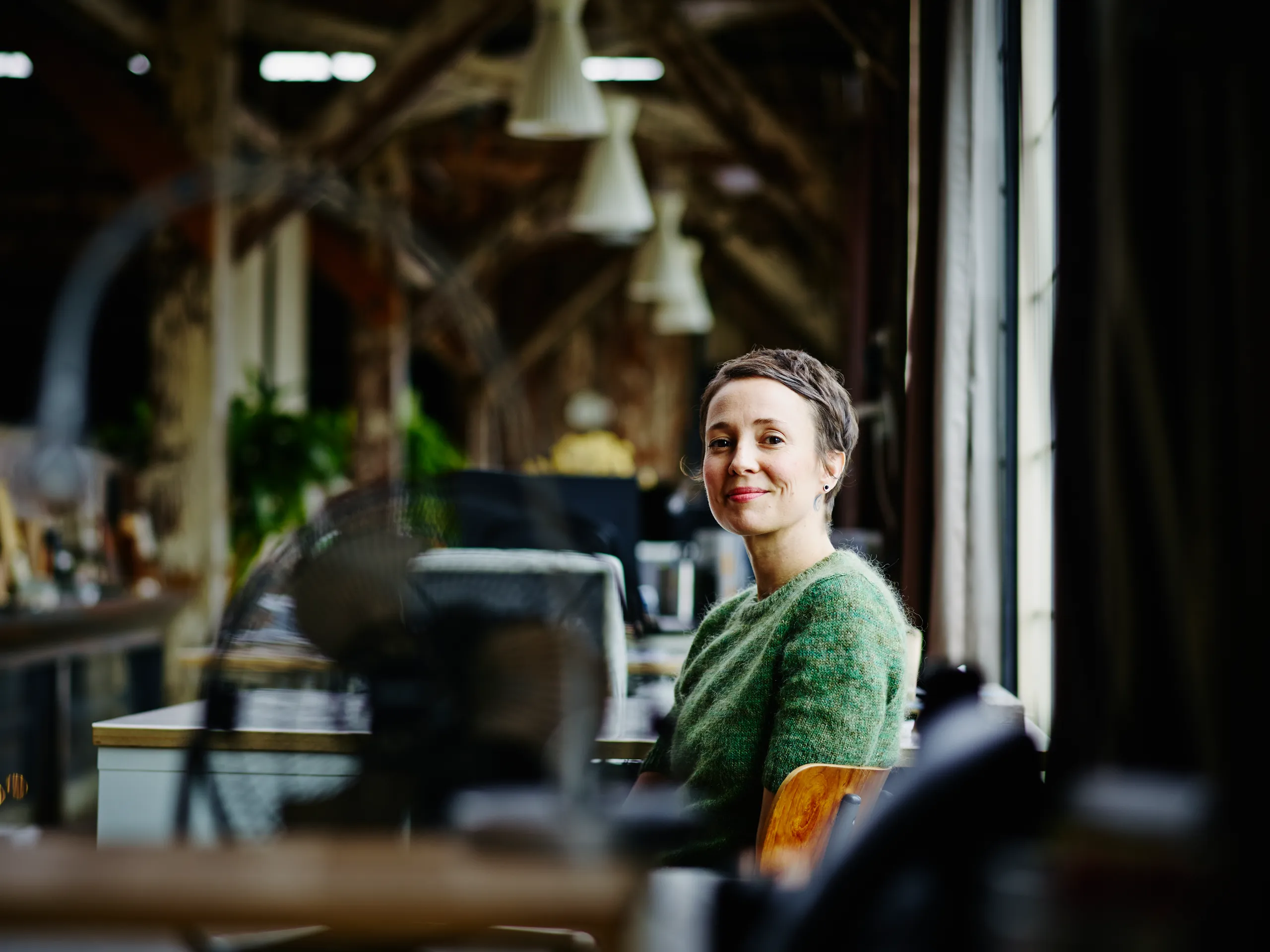 Smiling woman in a green cardigan sitting by a window in an office.
