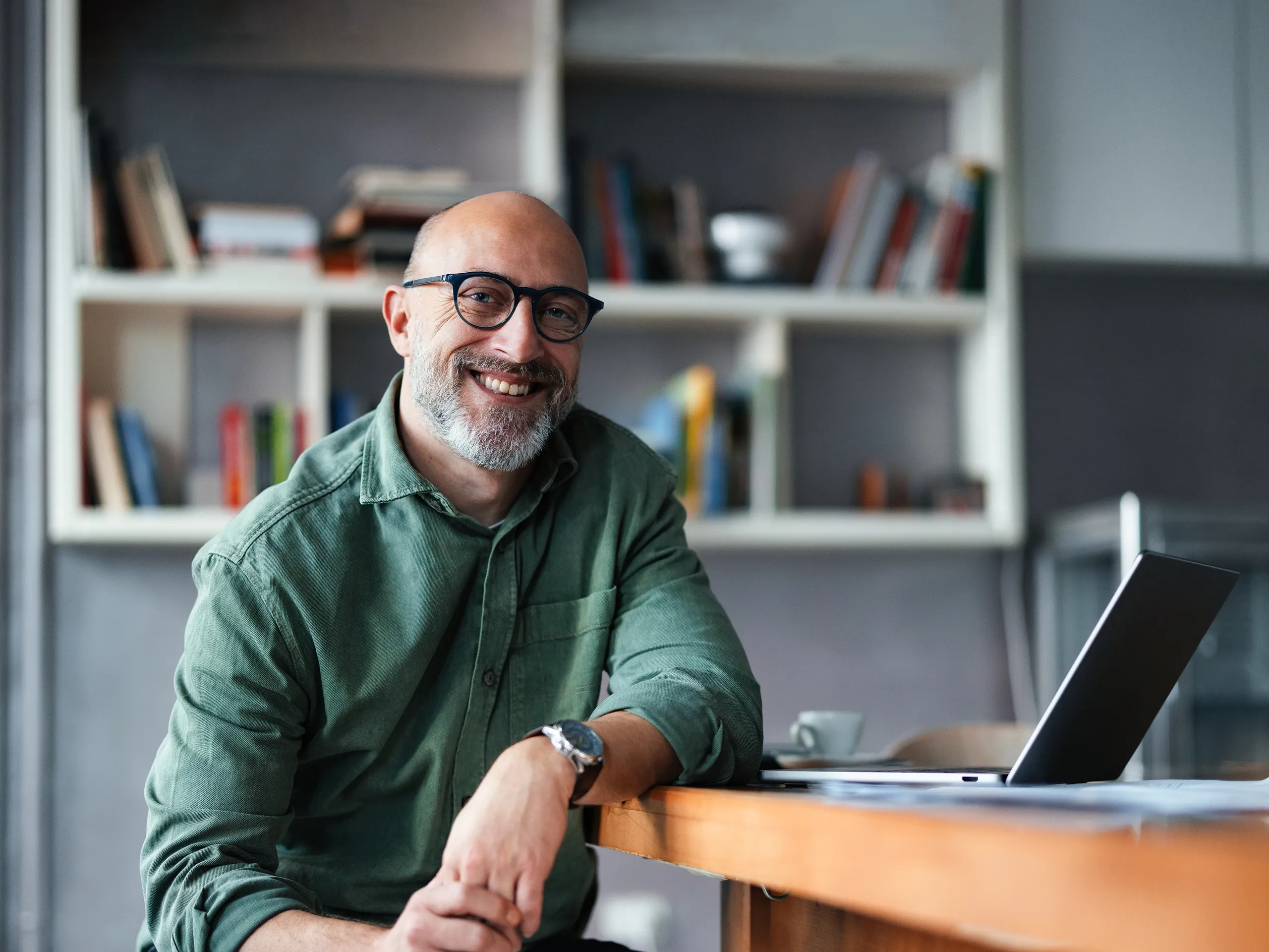 Person with glasses sitting at a desk with a laptop in a modern home office setting